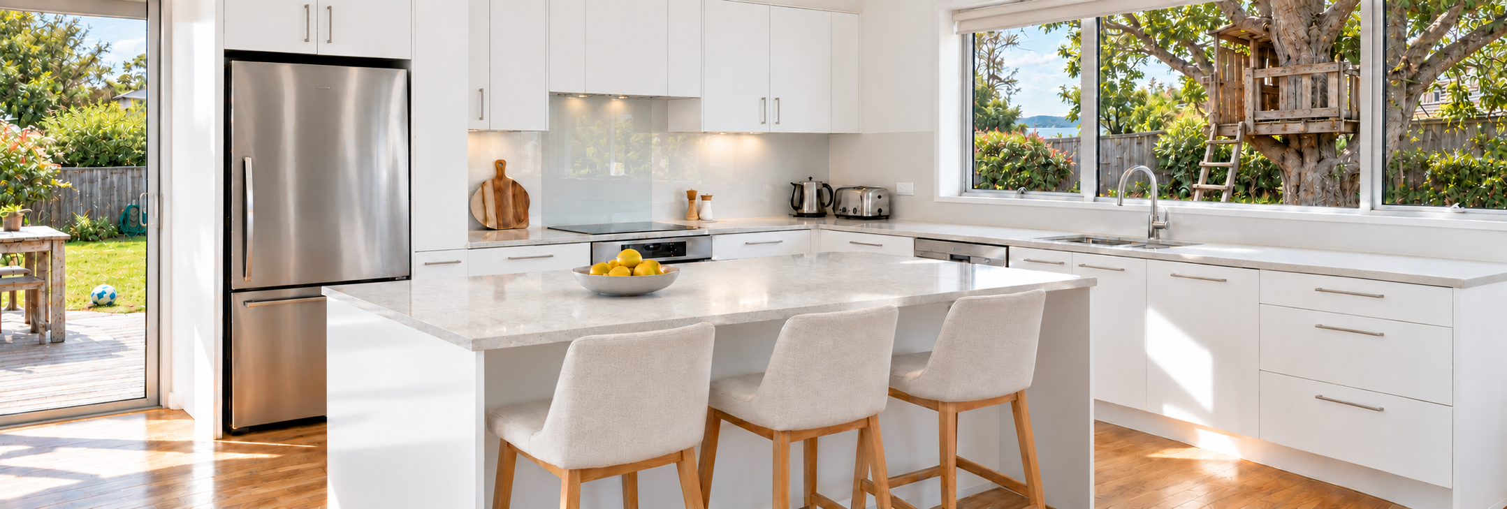 A bright white kitchen overlooking a family backyard with a timber treehouse